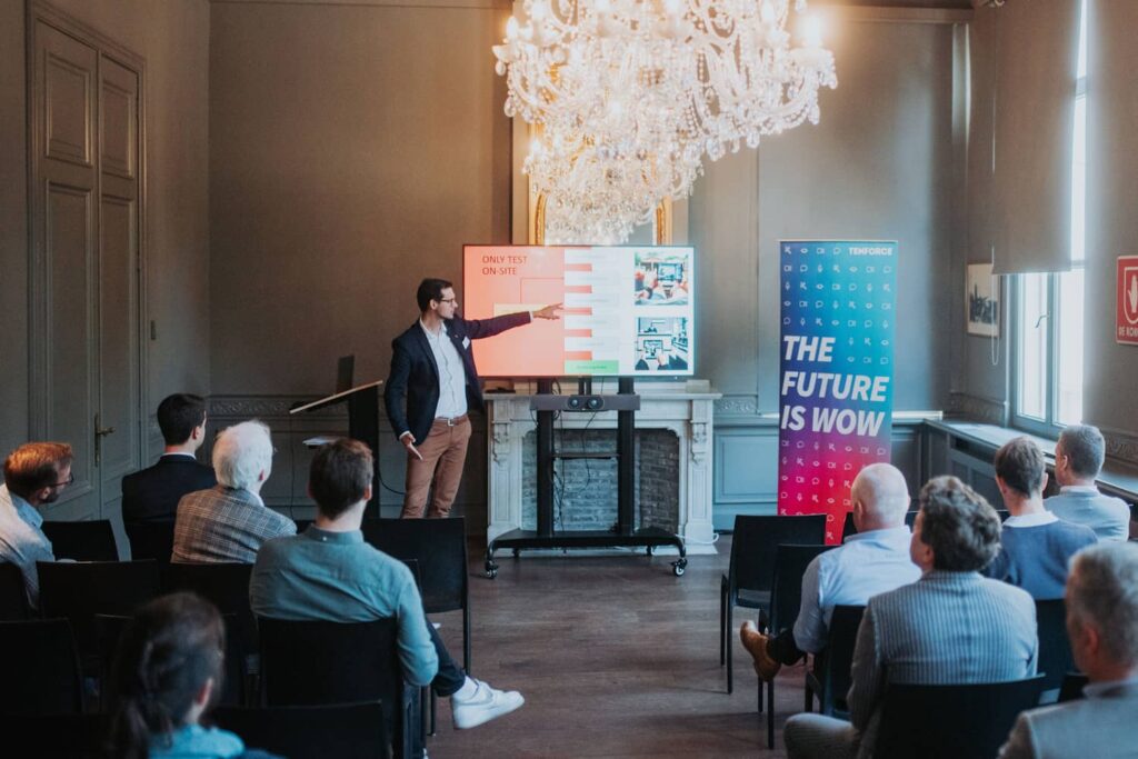 Christophe Jacobs from FLOWSPARKS stands at the front of a meeting room, presenting beside a large TV screen.