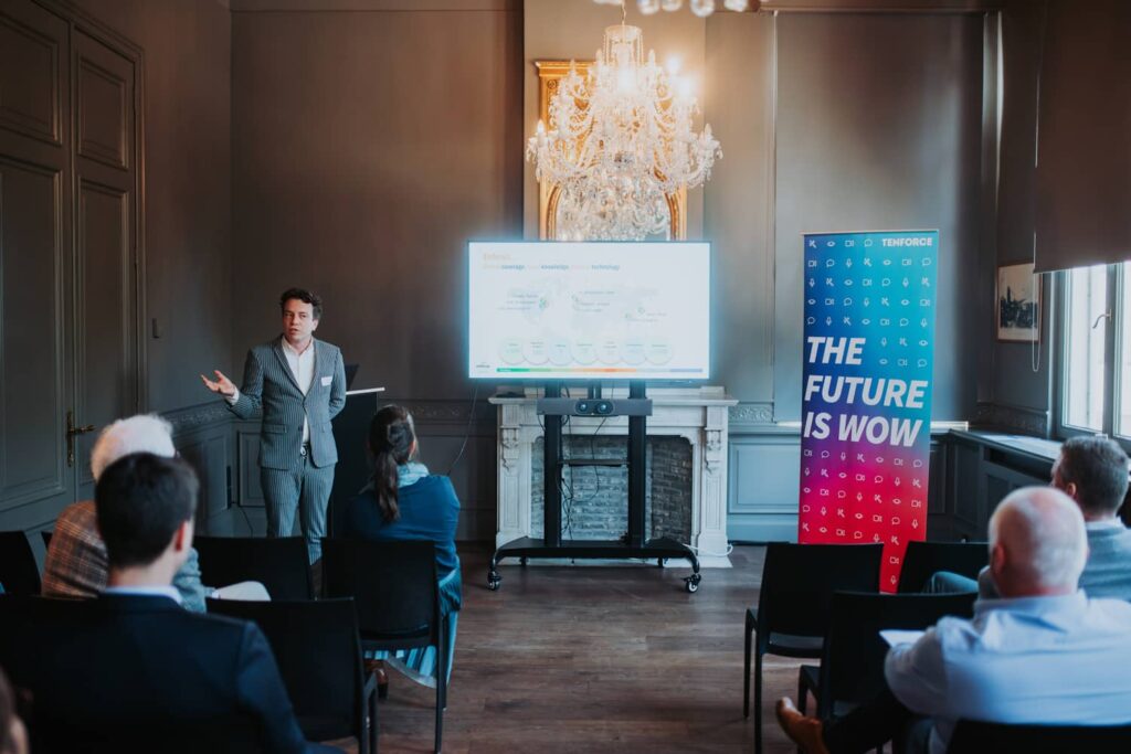 Michiel Scholberg from Enhesa stands at the front of a meeting room, presenting beside a large TV screen.