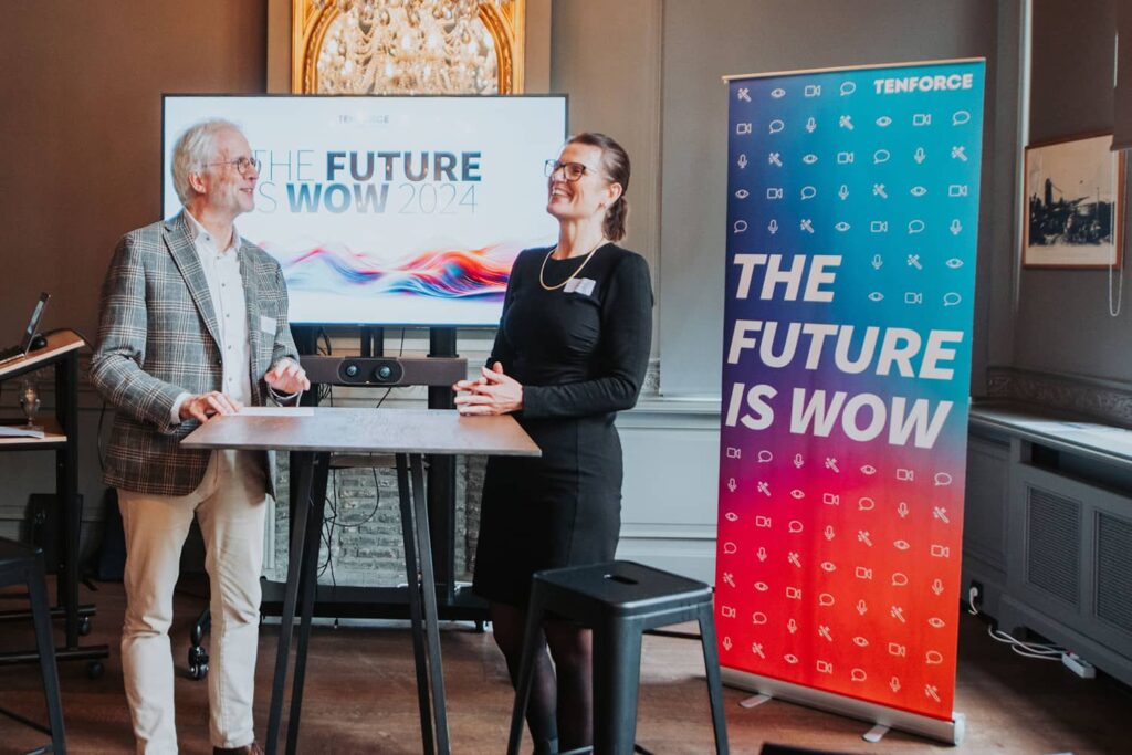 Bastiaan Debliek and Minna Kroger stand in conversation with a TV screen displaying The Future Is WOW behind them.