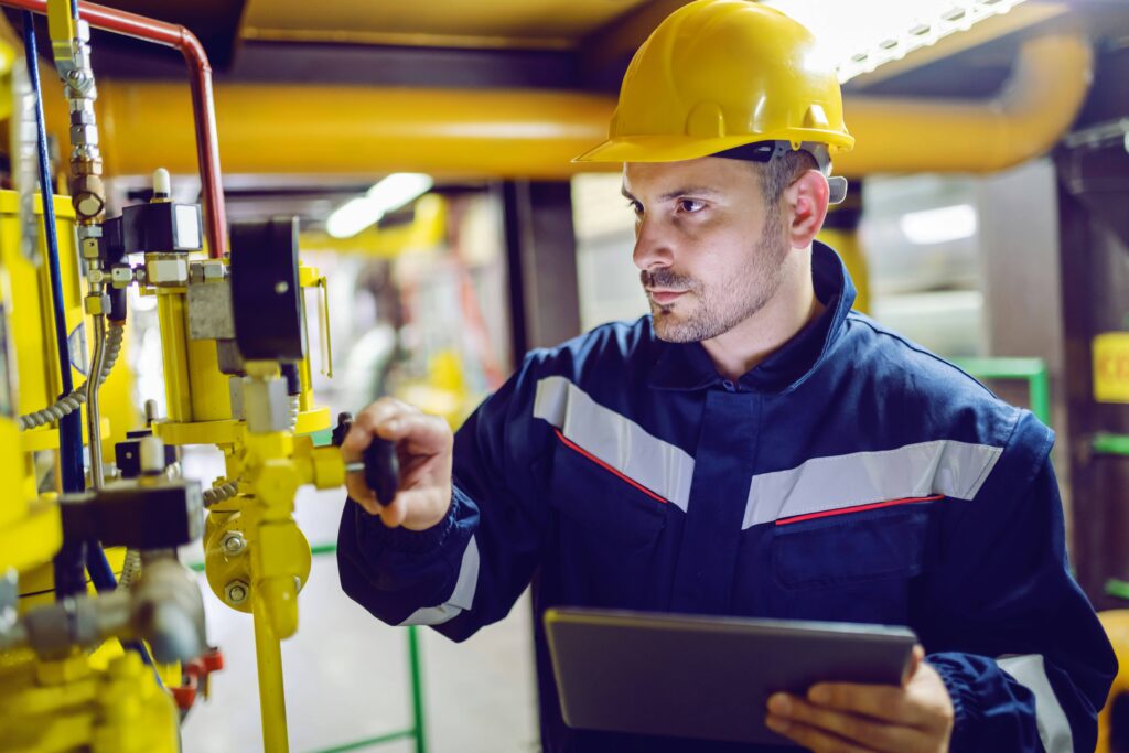 A man wearing a yellow hard hat and blue overalls checks piping at a chemical site as part of a Responsible Care audit.